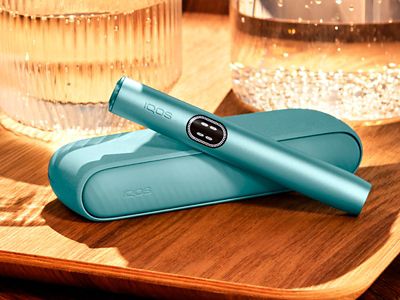 Устройство IQOS ILUMA i цвета Лазурный бриз над зарядным устройством на деревянном столе