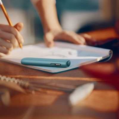 Mano sujetando IQOS Iluma i sobre cuaderno mientras se escribe.