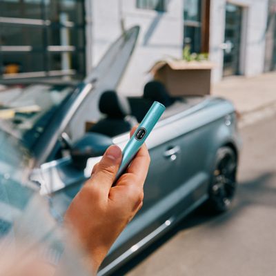 Persona usando IQOS Iluma i turquesa desde automóvil convertible en movimiento