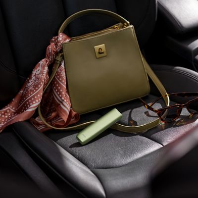 IQOS Iluma i ONE verde dentro de bolso beige sobre asiento del auto