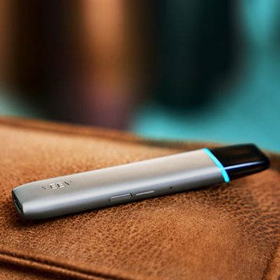 Ein VEEV ONE Device in Silky Grey liegt auf einer ledernen Oberfläche