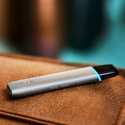 Ein VEEV ONE Device in Silky Grey liegt auf einer ledernen Oberfläche