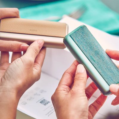 Zwei Personen halten einen IQOS ILUMA Pocktcharger in der Hand