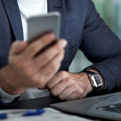 Mann im Anzug mit Handy in der Hand vor einem Laptop