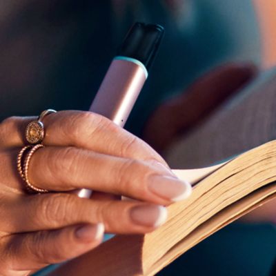 Eine Hand mit Ringen blättert in einem Buch und hält dabei ein VEEV ONE Device