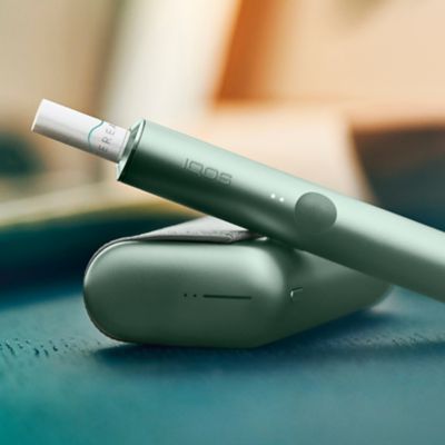 Ein IQOS ILUMA PRIME Device im Moss Green auf einem türkisen Notizbuch