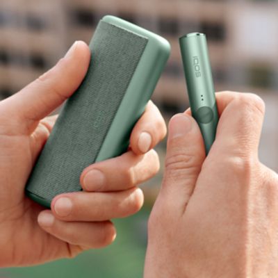 Jemand hält ein IQOS ILUMA Device und einen Pocketcharger in Moss Green in der Hand