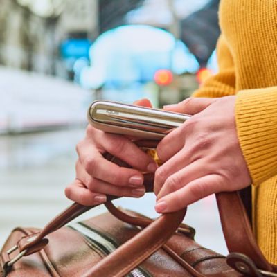 Jemand in einem gelben Pullover hält eine braune Tasche und ein IQOS ILUMA Kit in der Hand