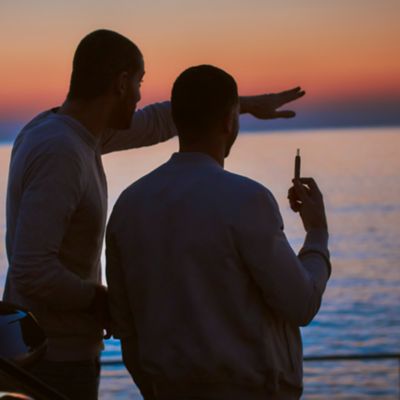 Zwei Personen stehen am Meer, einer hält eine E-Zigarette in der Hand