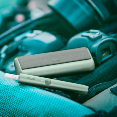 Ein IQOS ILUMA PRIME Device und Pocketcharger in Moss Green in einer Tasche mit Kamera-Equipment