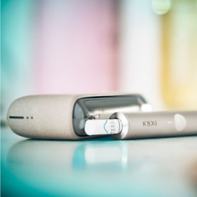 Ein IQOS ILUMA Device mit eingesetztem TEREA Tabakstick und ein Pocketcharger liegen auf einer spiegelnden Oberfläche