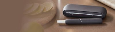 IQOS DUO Holder mit eingesetztem Tabakstick und IQOS Charger auf einem Tisch