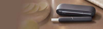 IQOS DUO Holder mit eingesetztem Tabakstick und IQOS Charger auf einem Tisch