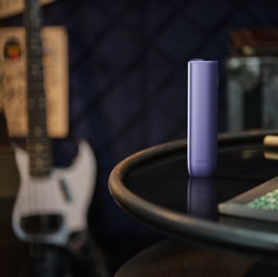 IQOS Iluma i Prime lila y guitarra eléctrica sobre mesa oscura.