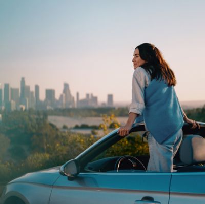 Mujer apoyada en un auto con un IQOS Iluma i ONE azul en la mano.