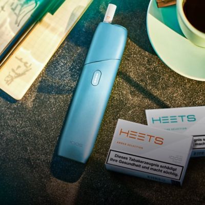 IQOS ORIGINALS ONE neben zwei Packungen HEETS Tabaksticks auf einem Tisch