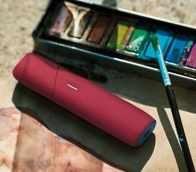 IQOS ORIGINALS DUO mit roter Silikon-Hülle vor einem Farbkasten