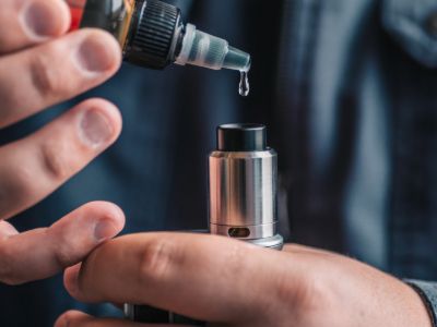 Vape tank being refilled with e-liquid from a dropper bottle.