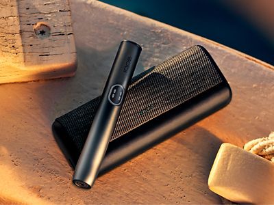 Устройство IQOS ILUMA i PRIME цвета Черный графит над зарядным устройством на белой поверхности