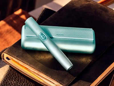 Устройство IQOS ILUMA i PRIME цвета Лазурный бриз над зарядным устройством на ноутбуке