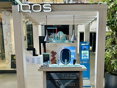 Dispositivos IQOS ILUMA ubicados dentro de exhibidor cilíndrico azul.