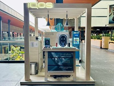 Primer plano de dispositivos IQOS ILUMA en vitrina circular turquesa.