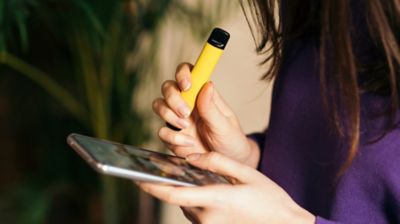 woman holding yellow vape and phone