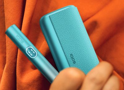 Zariadenie IQOS ILUMA v ruke na oranžovom pozadí