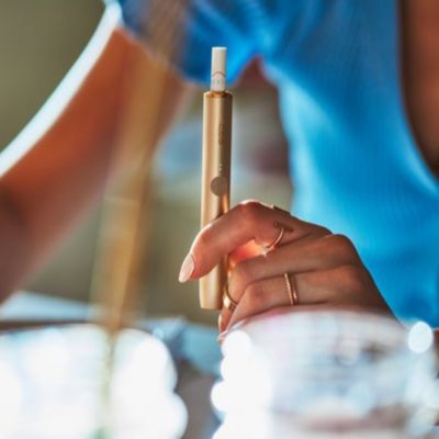 Žena držiaca zlaté zariadenie IQOS pri počítači.