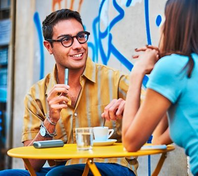 Muž so zariadením IQOS Iluma v ruke sediaci na káve, zabávajúci sa so ženou