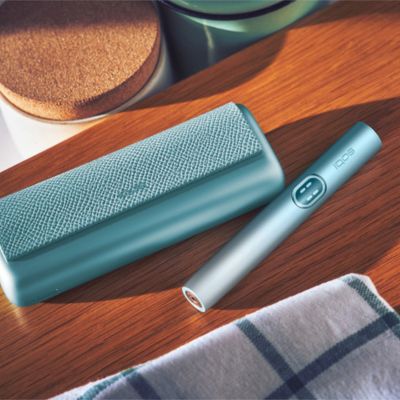 A person placing a jade green IQOS ILUMA PRIME Holder into a Pocket Charger covered with a full wrap.