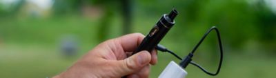 Vape picture showing a small vape device being charged with a portable power bank outdoors.