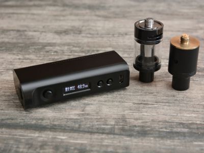 Vape picture comparing different vape sizes, showing a compact vape mod and two atomisers on a wooden surface.