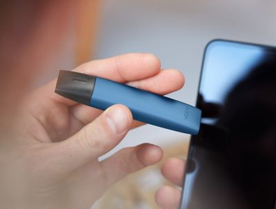 Osoba držící zařízení IQOS VEEV a mobilní telefon