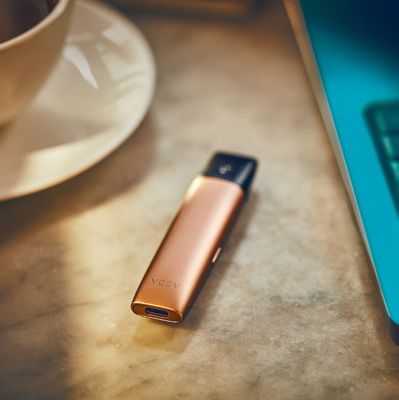 Copper IQOS VEEV sitting on the tabletop next to a laptop and a coffee cup.