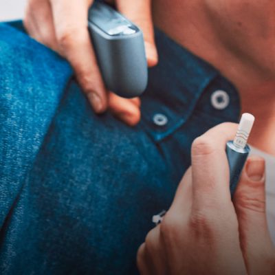 Jemand im Jeanshemd hält ein IQOS ILUMA und einen Pocketcharger in der Hand