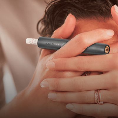 Jemand hält jemandem die Augen zu und hat dabei ein IQOS ILUMA in der Hand