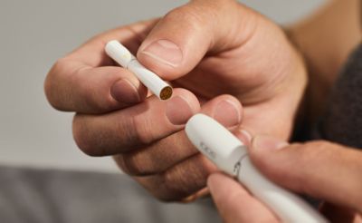 Hand führt Tabakstick in weißen IQOS DUO Holder ein