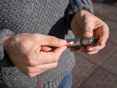 Person holding a zero-nicotine vape device connected to its charger