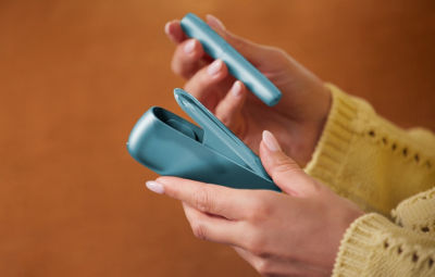 Hände halten IQOS Originals Duo Holder und Pocket Charger in türkiser Farbe.
