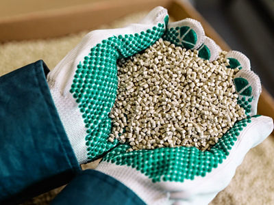 Ruce v rukavicích drží recyklovaný materiál ze zařízení. 